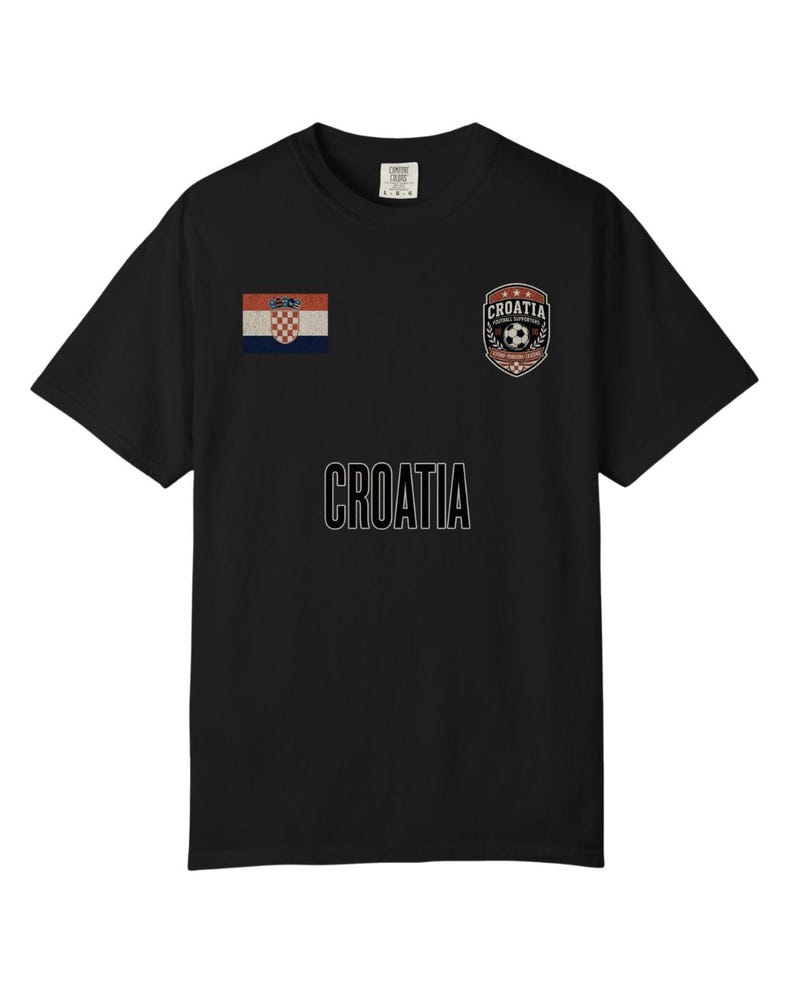 May include: Black t-shirt featuring the word "CROATIA" in white block letters. The shirt has a Croatian flag patch on the left sleeve and a "CROATIA" crest with a soccer ball on the right chest.