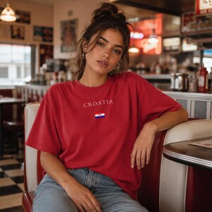 Peut inclure: Un t-shirt rouge avec le mot "CROATIA" imprim&eacute; en blanc au-dessus d'un petit drapeau croate. Le t-shirt est &agrave; manches courtes et semble &ecirc;tre fait d'une mati&egrave;re douce. La personne porte un jean bleu.