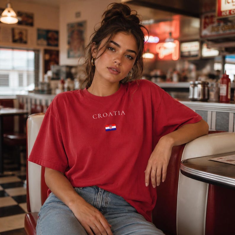 Peut inclure: Un t-shirt rouge avec le mot "CROATIA" imprim&eacute; en blanc au-dessus d'un petit drapeau croate. Le t-shirt est &agrave; manches courtes et semble &ecirc;tre fait d'une mati&egrave;re douce. La personne porte un jean bleu.