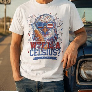 May include: A white t-shirt featuring a graphic of a bald eagle wearing American flag sunglasses and holding a glass bottle. The text reads "WTF IS A CELSIUS?" in red and blue lettering, surrounded by firework illustrations and small stars.