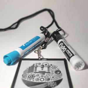 May include: A black lanyard with two markers attached. One marker is blue and says "dry erase". The other marker is white and says "Expo low odor". A black and white badge with a graphic design is also attached to the lanyard.