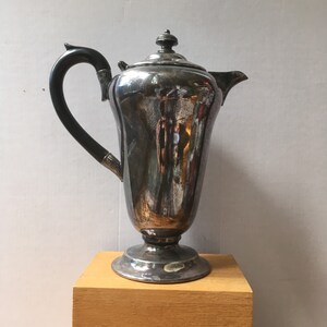 May include: A silver teapot with a black handle and a round, ornate base. The teapot has a shiny, reflective surface.