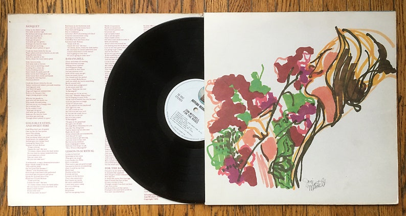 May include: A white vinyl record album cover with a colorful abstract painting of a woman smelling flowers. The album title is "For the Roses" by Joni Mitchell.