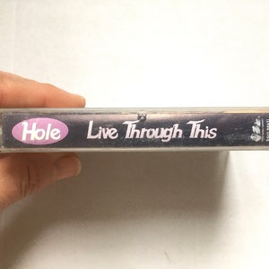 May include: A clear plastic cassette tape case with a black background and white text. The text reads "Hole Live Through This".