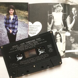 May include: A black cassette tape with the title "HOLE - LIVE THROUGH THIS" and the song titles "VIOLET", "MISS WORLD", "PLUMP", "ASKING FOR IT", "JENNIFER'S BODY", "DOLL PARTS" printed on the label. The cassette tape is on top of a booklet with black and white photos of the band members.