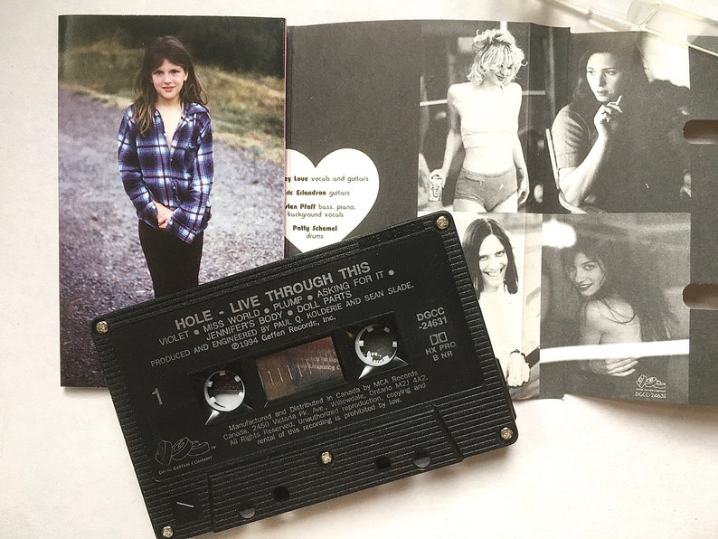 May include: A black cassette tape with the title "HOLE - LIVE THROUGH THIS" and the song titles "VIOLET", "MISS WORLD", "PLUMP", "ASKING FOR IT", "JENNIFER'S BODY", "DOLL PARTS" printed on the label. The cassette tape is on top of a booklet with black and white photos of the band members.