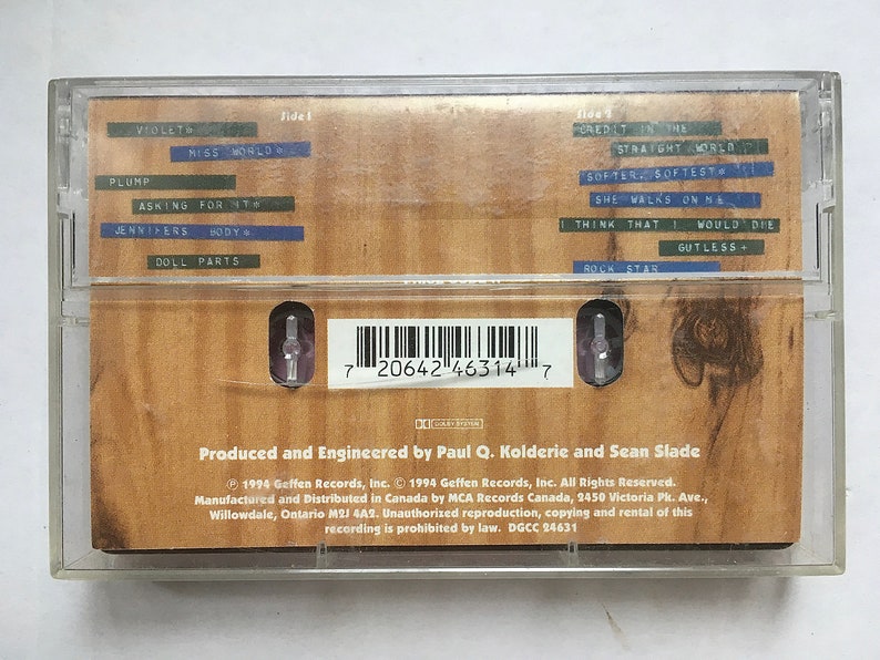 May include: A cassette tape with a brown woodgrain background. The tape is labeled with the title "Credit in the Straight World" and the artist "Miss World". The track list includes "Violet", "Plump", "Asking for It", "Jennifers Body", "Doll Parts", "Softer, Softest", "She Walks on Me", "I Think That I Would Die", "Gutless", and "Rock Star".
