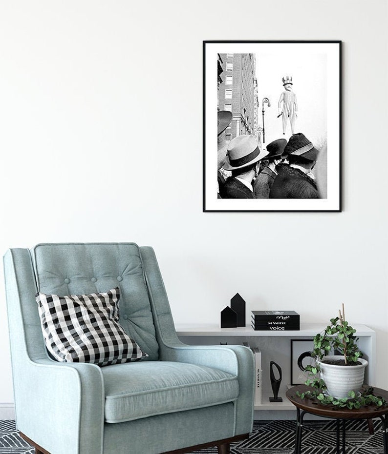 May include: Black and white photograph of three people in hats looking up at a person in a striped outfit and a crown standing on a street corner.