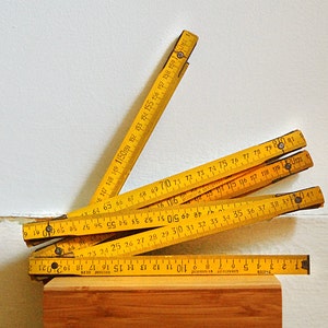 May include: A set of yellow wooden folding rulers with black markings and numbers. The rulers are stacked on top of each other and are partially folded.