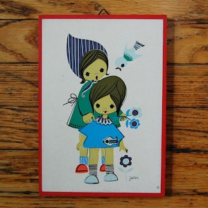 May include: A vintage illustration of two girls with blue and green clothing, holding flowers and a bird. The illustration is on a white background with a red border and the text "Jokilien" at the bottom.