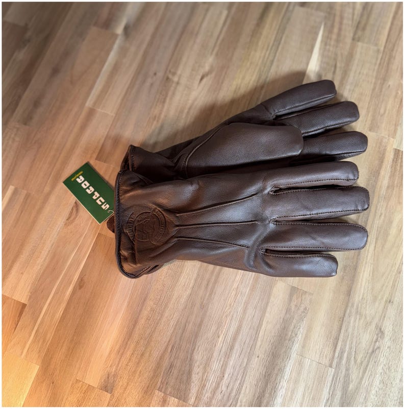 May include: A pair of brown leather gloves with a stitched design on the back of the hand. The gloves are folded in half and the tag reads "SOCKS"