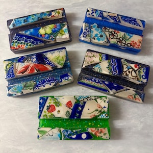 May include: A collection of five rectangular soap dishes. Each dish is decorated with a mosaic of broken ceramic pieces in shades of blue, white, green, and red. The dishes have a glittery finish.
