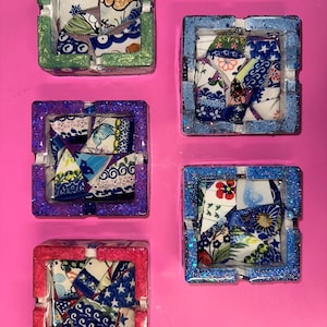 May include: Four square ceramic ashtrays with different colored borders. Each ashtray has a mosaic design of broken pieces of blue and white china.