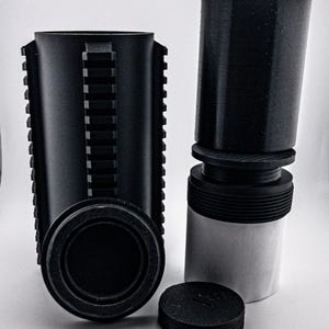 May include: Black cylindrical components with various textures and designs. One component has a series of vertical ridges, while another has a threaded base. A detached lid and a smaller cylindrical piece are also present.