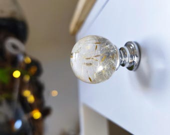 May include: A clear, spherical cabinet knob with a silver base, filled with dried dandelion seeds. The knob is attached to a white cabinet door, offering a natural and unique design element.