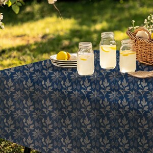 May include: A blue tablecloth with a white leaf pattern. Three glass jars filled with lemonade are on the table, along with a plate of lemons and a stack of white plates.