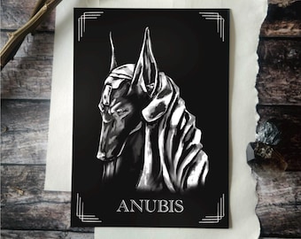 May include: A black and white art print featuring the Egyptian god Anubis. The artwork depicts Anubis with a dog-like head and a detailed, stylized design. The word "ANUBIS" is printed in white at the bottom of the print.