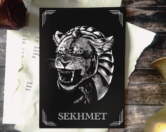 May include: Black and white Sekhmet art print. The image features a detailed illustration of a lioness with an Egyptian headdress, set against a black background. The word "SEKHMET" is printed at the bottom in white.