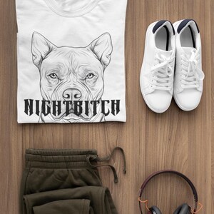 Può includere: Maglietta bianca con un'illustrazione in bianco e nero di una testa di pit bull e il testo "Night Bitch". La maglietta è abbinata a pantaloni della tuta verde oliva, scarpe da ginnastica bianche e cuffie bordeaux.