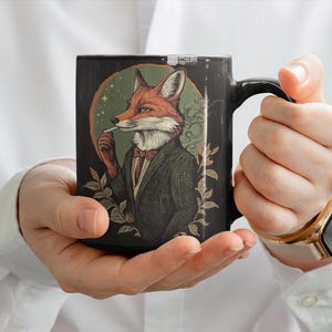 May include: Black ceramic mug with a graphic of a fox wearing a suit and smoking a cigarette. The fox has orange fur and a white collar. The background is a dark green with leaves.
