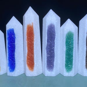 Könnte beinhalten: Sieben weiße Kristallspitzen mit verschiedenen farbigen Einschlüssen. Die Farben sind gelb, blau, orange, lila, grün und braun.