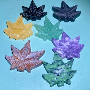 Puede incluir: Siete pisapapeles de piedra en forma de hoja de diferentes colores. Las hojas son en tonos de verde, morado, rojo, amarillo y negro.