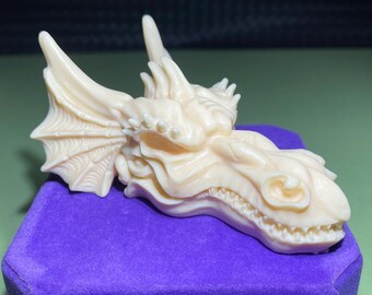 May include: A detailed, cream-colored dragon head sculpture with intricate wing details. The sculpture is made of a smooth, polished material and has a realistic appearance.