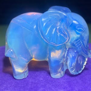 May include: A small, blue glass elephant figurine. The elephant is made of translucent glass and has a slightly iridescent finish.
