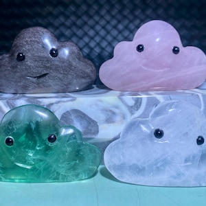 Può includere: Quattro piccole sculture di nuvole intagliate a mano in diversi tipi di pietra. Le nuvole hanno occhi neri e una bocca sorridente. Le nuvole sono di colore grigio, rosa, verde e bianco.