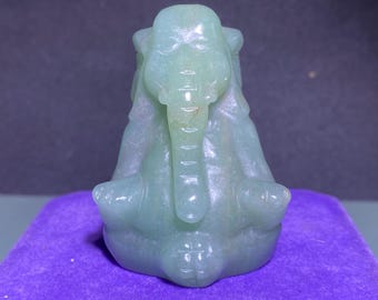 Puede incluir: Una figurita de elefante de jade verde sentada en una postura meditativa con la trompa levantada. La figurita está tallada con detalles intrincados y tiene un acabado liso y pulido.