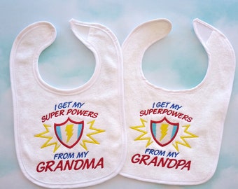 May include: Two white baby bibs with embroidered text. The bib on the left says "I get my super powers from my grandma". The bib on the right says "I get my superpowers from my grandpa".