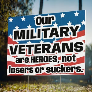 May include: A red, white, and blue American flag with stars printed on a blue background. The text on the sign reads "Our Military Veterans are heroes, not losers or suckers."
