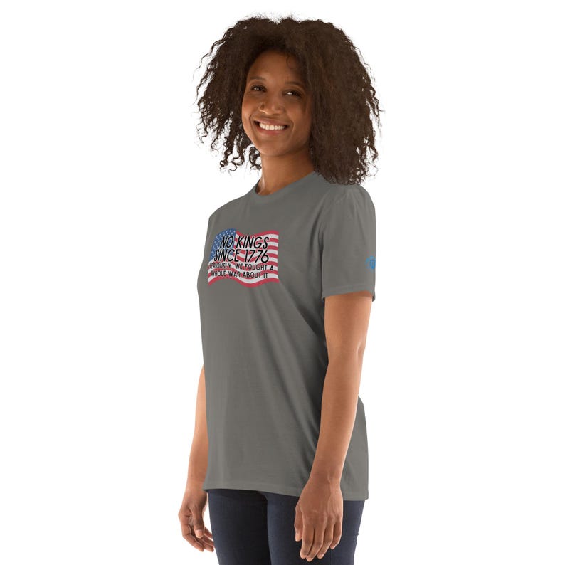 Puede incluir: Una camiseta gris con el texto "NO KINGS SINCE 1776" en un dise&ntilde;o rectangular con un gr&aacute;fico de bandera roja, blanca y azul. La camiseta es de cuello redondo y manga corta.