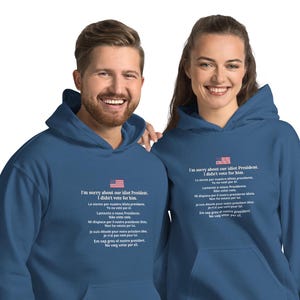 May include: Two people wearing matching navy blue hooded sweatshirts. The sweatshirts have the text "I'm sorry about our idiot President. I didn't vote for him" in white, along with the American flag.