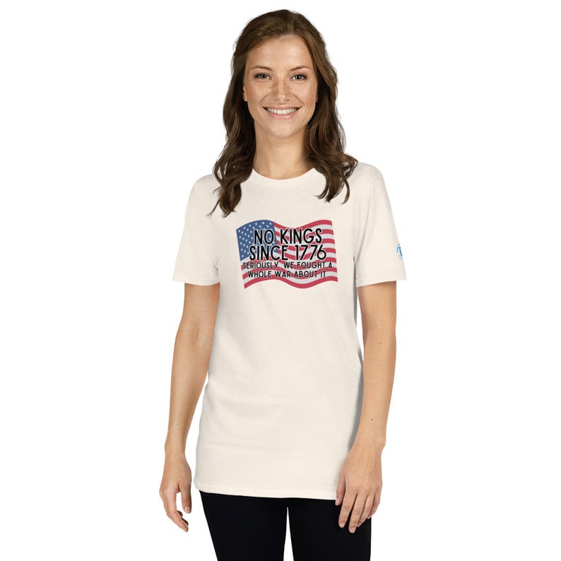 Puede incluir: Camiseta color crema con la bandera estadounidense y el texto "NO KINGS SINCE 1776". La camiseta tambi&eacute;n incluye la frase "SERIOUSLY, WE FOUGHT A WHOLE WAR ABOUT IT". El dise&ntilde;o est&aacute; impreso en rojo, blanco y azul.