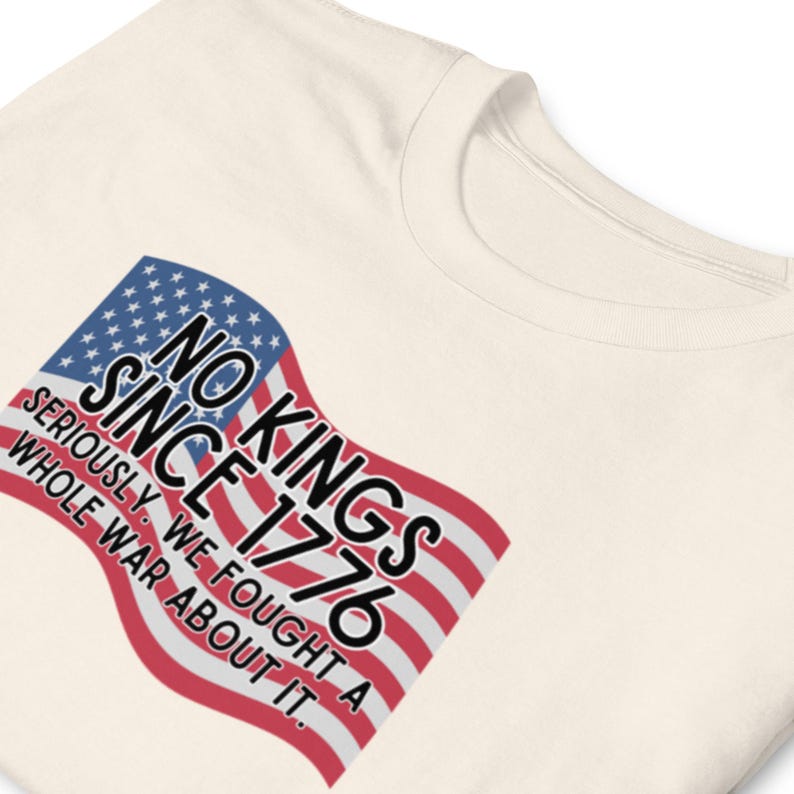 Puede incluir: Camiseta color crema con un dise&ntilde;o de la bandera estadounidense y el texto "NO KINGS SINCE 1776". El texto tambi&eacute;n incluye "SERIOUSLY, WE FOUGHT A WHOLE WAR ABOUT IT."