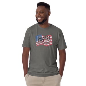 Puede incluir: Una camiseta gris con la bandera estadounidense y el texto "NO KINGS SINCE 1776. SERIOUSLY WE FOUGHT A WHOLE WAR ABOUT IT." La camiseta est&aacute; hecha de un material suave.