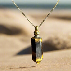May include: A gold-colored chain necklace with a pendant. The pendant is a faceted, rectangular shape with a pointed bottom. The pendant has a tiger's eye stone appearance, with bands of brown and yellow. The necklace is displayed on a neutral background.