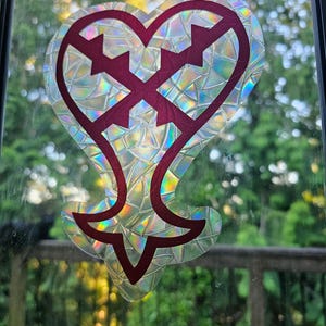 May include: A holographic sticker of a red heart with a cross inside, on a glass window.