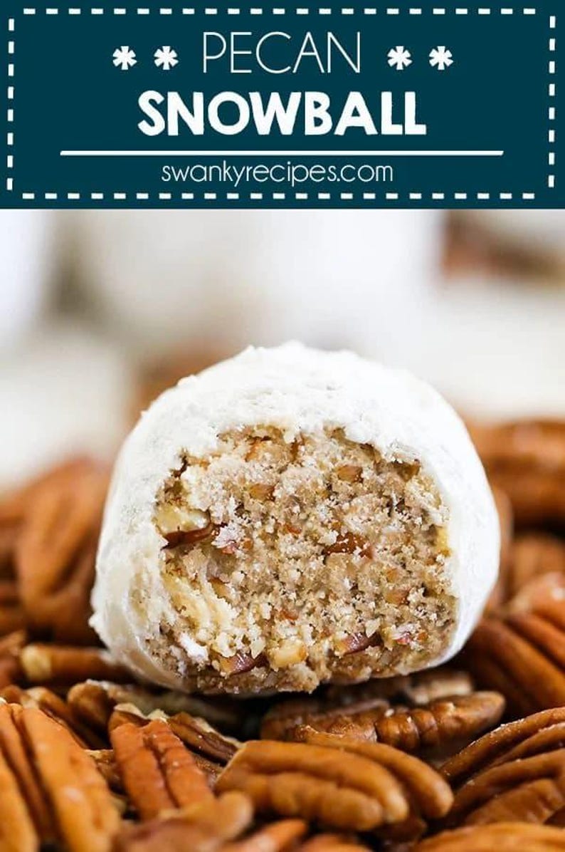 May include: A pecan snowball cookie, dusted with powdered sugar, is shown with a bite taken out, revealing the pecan filling. The cookie is sitting on a bed of pecan halves.