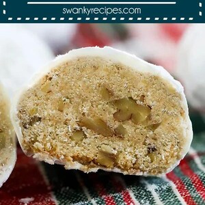 May include: A close-up of a pecan snowball cookie cut in half, revealing the pecan pieces inside. The cookie is covered in white icing and is sitting on a red and green striped napkin. The text "PECAN SNOWBALLS" is displayed above the cookie.