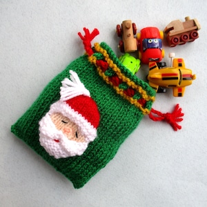 Può includere: Un sacco di Babbo Natale di maglia verde con barba bianca e cappello rosso, pieno di macchinine giocattolo e un aereo giocattolo.