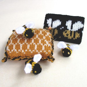 May include: A knitted pincushion shaped like a honeycomb with three small knitted bees. The pincushion is brown and white and the bees are black and yellow with white wings.