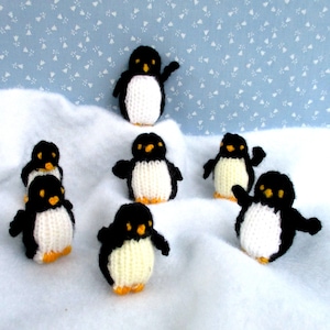 May include: A collection of handmade knitted penguin figurines. Each penguin has a black body, white belly, and orange feet and beak. The penguins are arranged on a white, textured surface against a light blue background with a floral pattern.