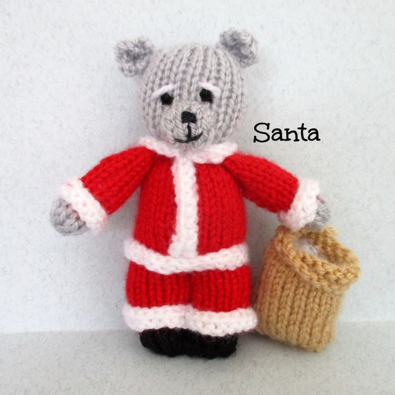 May include: A gray knitted teddy bear dressed as Santa Claus, wearing a red suit with white trim and holding a brown knitted bag. The text "Santa" is written in black on a white background.