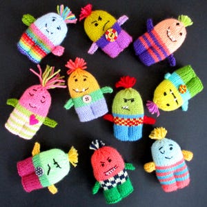 May include: Ten colourful knitted finger puppets with different facial expressions and designs. The puppets are made with a variety of colours, including pink, green, blue, yellow, and orange. Each puppet has a unique personality and features, such as a heart, a button, or a striped pattern.