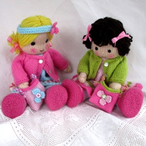 May include: Two knitted dolls wearing pink and green cardigans and matching pink shoes. The dolls are holding pink and green purses with flower accents.