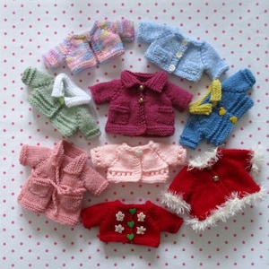 May include: A collection of ten knitted baby sweaters in various colours, including pink, red, blue, green, and purple. The sweaters are all different styles, with some having buttons, some having collars, and some having pockets.