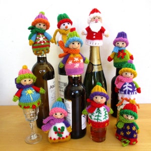 Könnte beinhalten: Eine Sammlung bunter, gestrickter Flaschenverschlüsse mit verschiedenen Weihnachtsfiguren, darunter der Weihnachtsmann, ein Schneemann und ein Pinguin. Die Verschlüsse sind auf Wein- und Champagnerflaschen platziert.