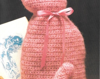 May include: A pink crocheted cat with a pink ribbon around its neck. The cat is sitting on a book with a gold key next to it. The text "Favorite Feline!" is written above the cat.